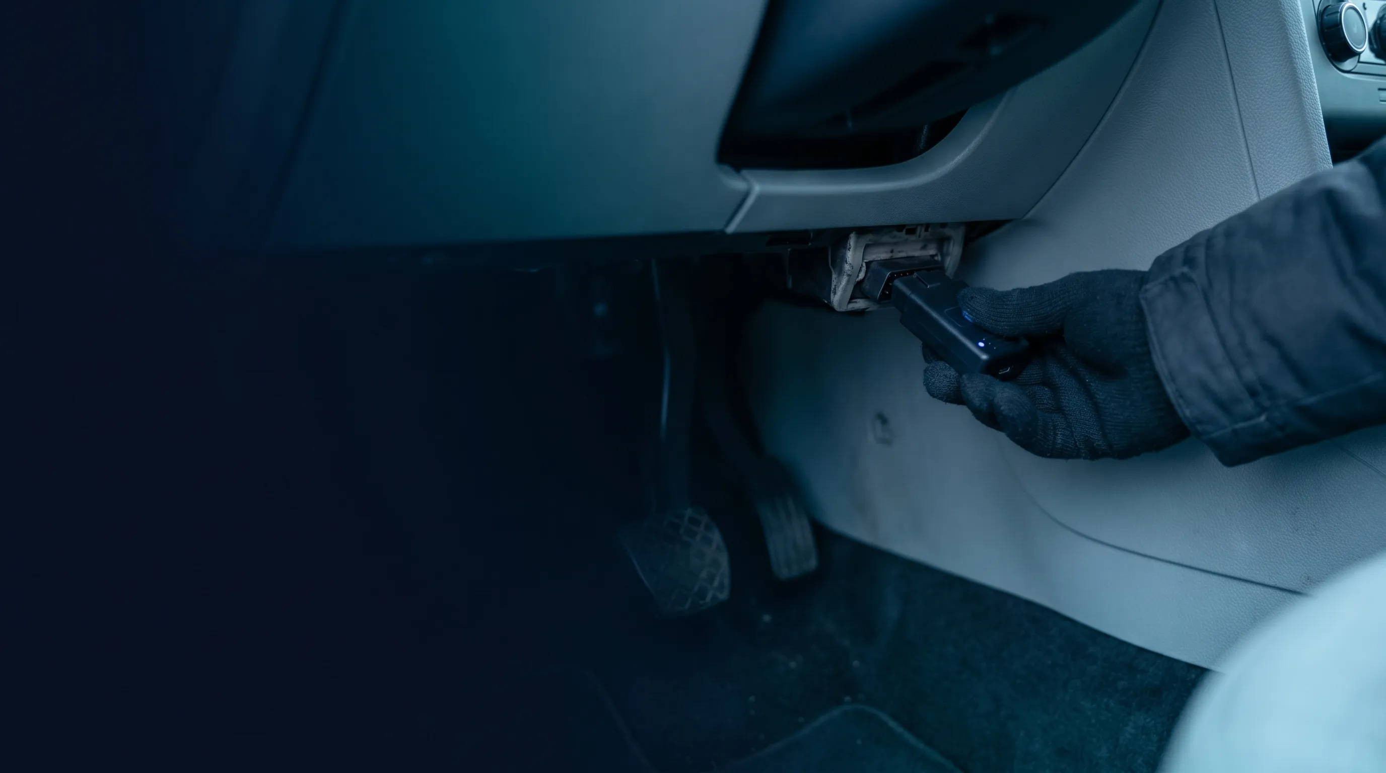 Disponentin steckt einen kompakten OBD-II-Tracker in den Diagnose-Anschluss eines Sprinter-Transporters auf einem deutschen Hof in der blauen Stunde