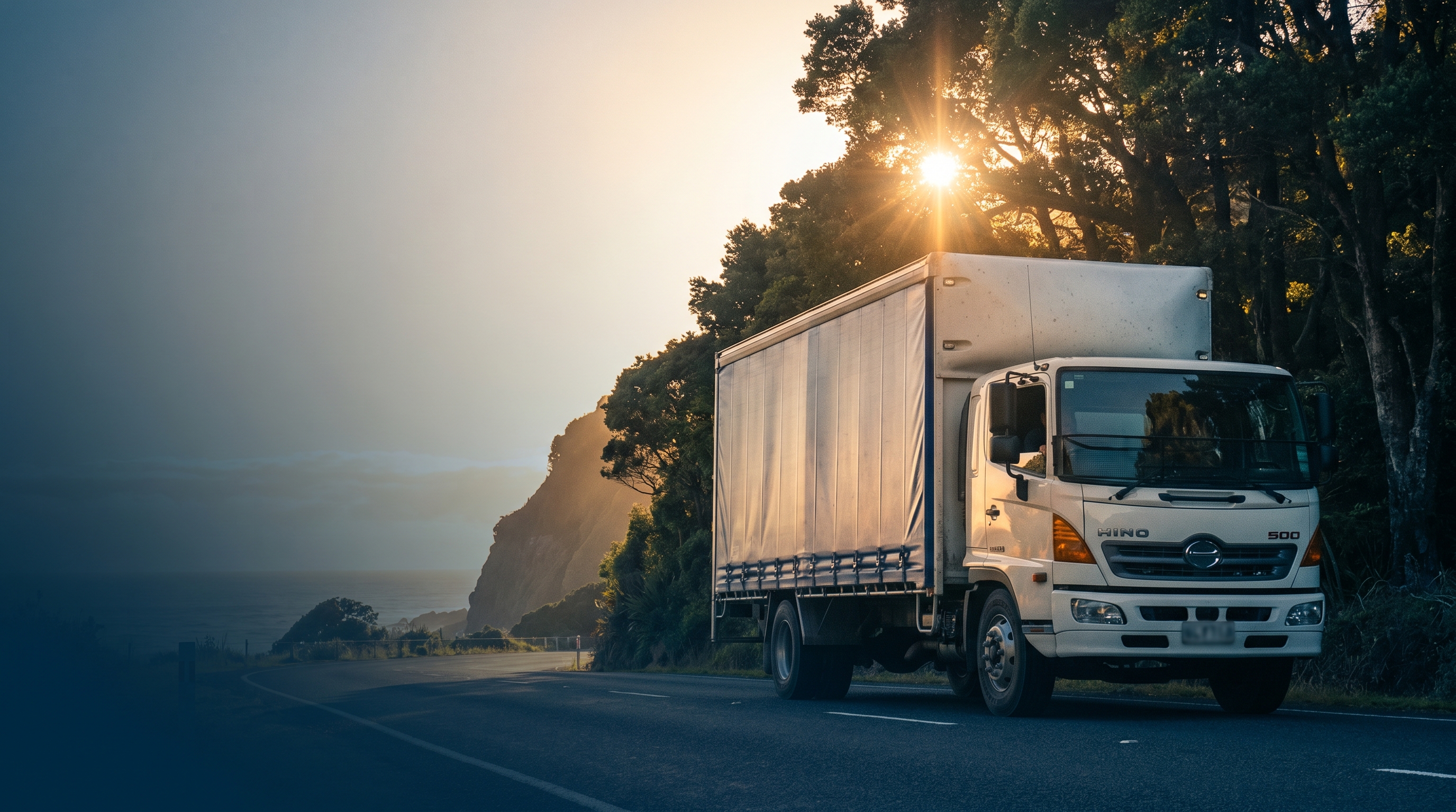 NZ commercial fleet vehicles on a rural state highway at golden hour with green Canterbury Plains landscape